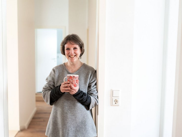 Ältere Frau steht in einer neuen Wohnung mit einer Tasse Kaffee in der Hand